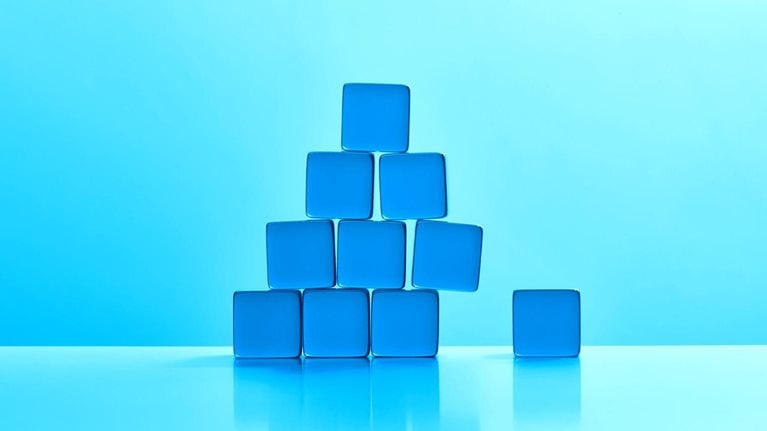 A triangular stack of blue acrylic cubes. The bottom right cube has been removed and causing the stack to become unstable.