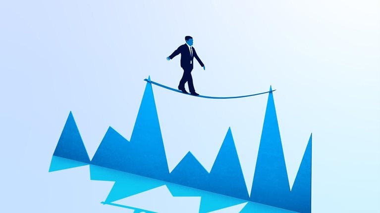 A businessman balancing on a tightrope tied between two peaks of a graph