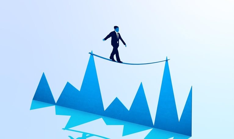 A businessman balancing on a tightrope tied between two peaks of a graph