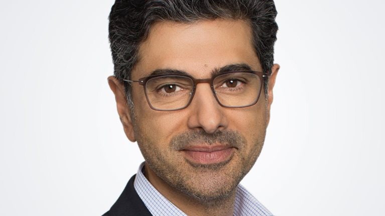 A photograph captures Alok Sama in a suit jacket and button down shirt, smiling gently against a white background.