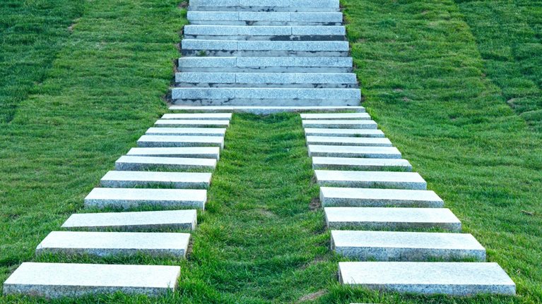 Two stone paths come together to create a staircase that leads up a grassy hill.