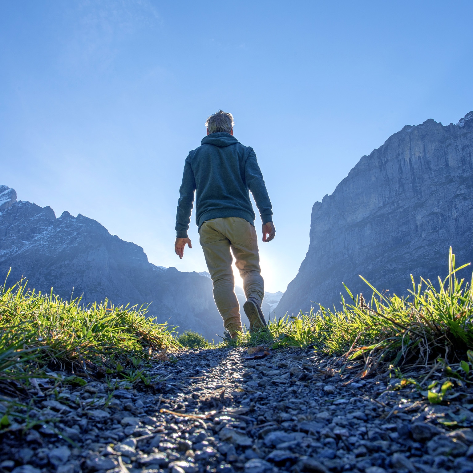 Person hiking up a path through a grassy mountain ridge at sunrise.