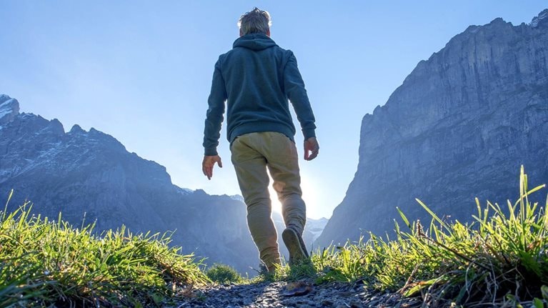 Person hiking up a path through a grassy mountain ridge at sunrise.