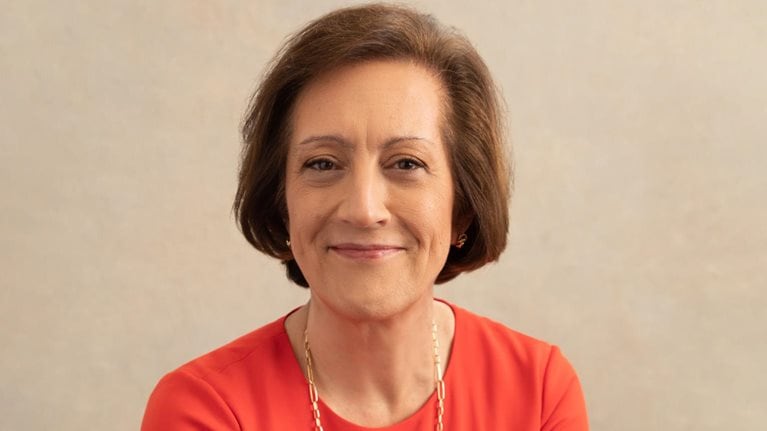 A smiling Judy Marks in a sophisticated red fitted top and a gold link chain around her neck.