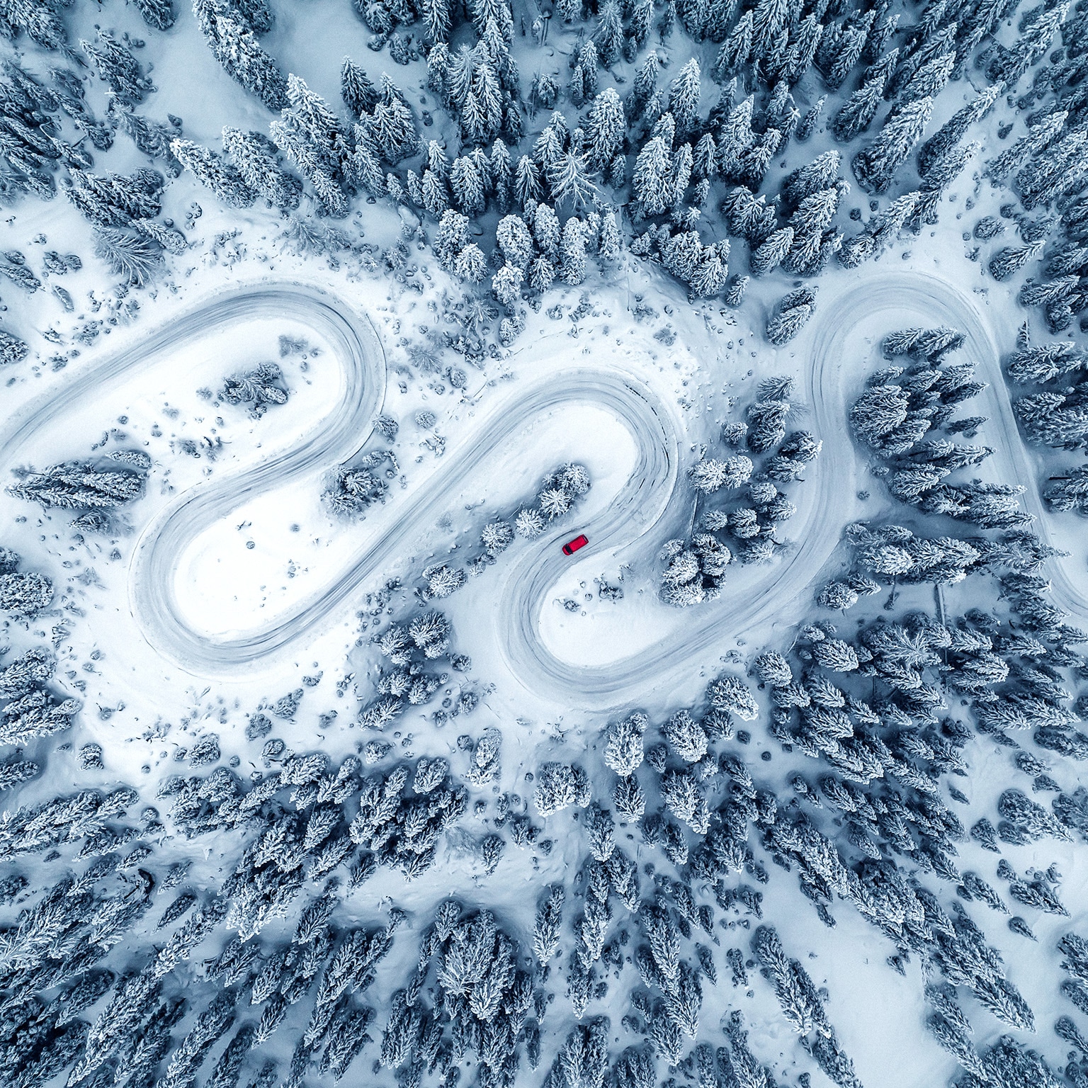 Drone image directly above a camper van crossing a winding road through a snow covered forest, Dolomites, Italy