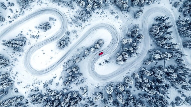 Drone image directly above a camper van crossing a winding road through a snow covered forest, Dolomites, Italy