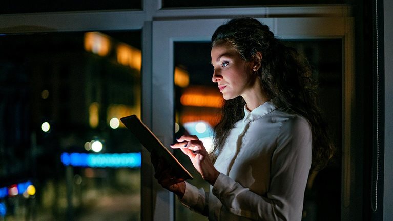 Image of a businesswoman working late on a digital tablet in an office.