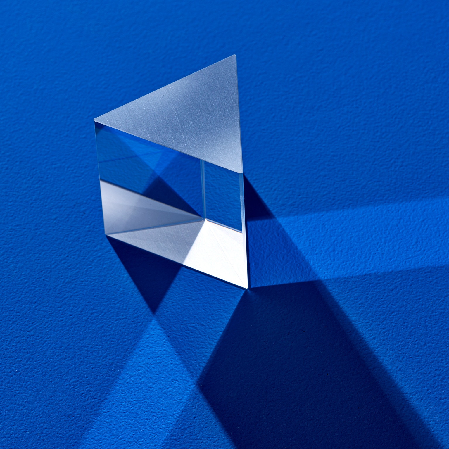 Triangular prism refracting light beam on blue colored background.