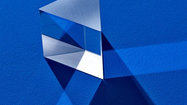 Triangular prism refracting light beam on blue colored background.