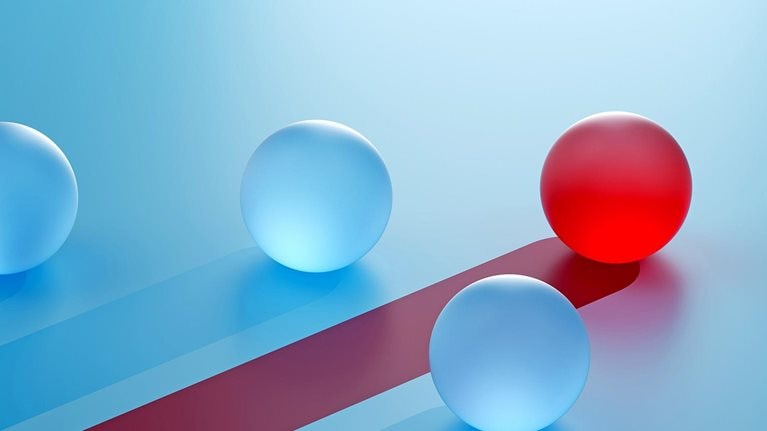 A single red sphere breaks away from identical blue spheres, moving on a distinct path. It symbolizes competitive advantage—standing out through differentiation, focus, and strategic direction.