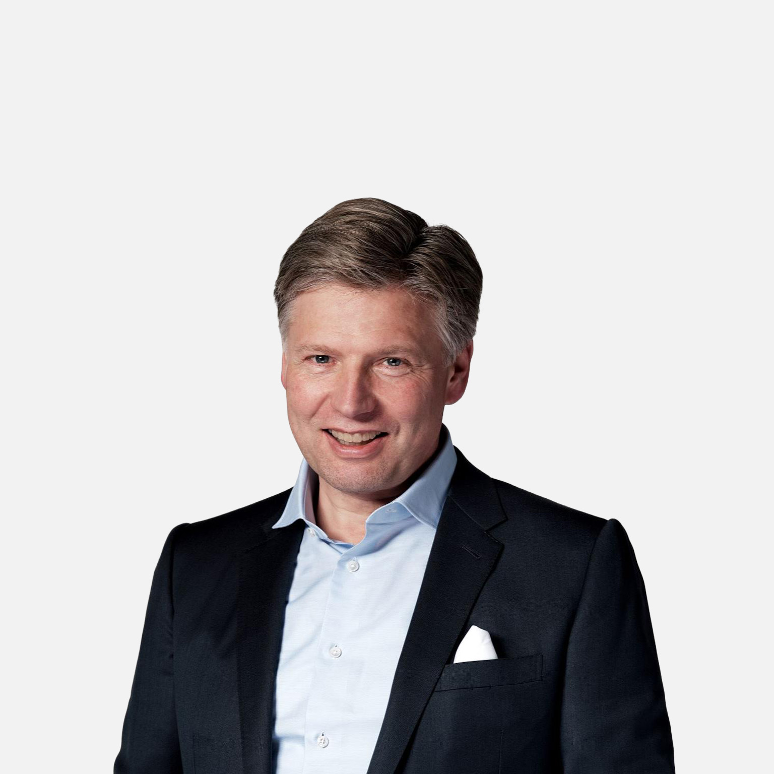 A studio-style portrait of a smiling Sven Smit wearing a dark suit jacket, light blue shirt, and white pocket square against a plain light background. 