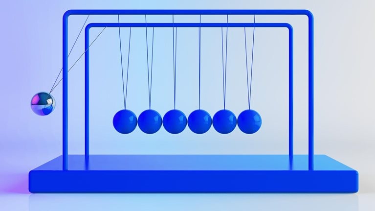 Newton's Cradle, with shiny, metallic balancing balls. Six remain still as one is in motion. 