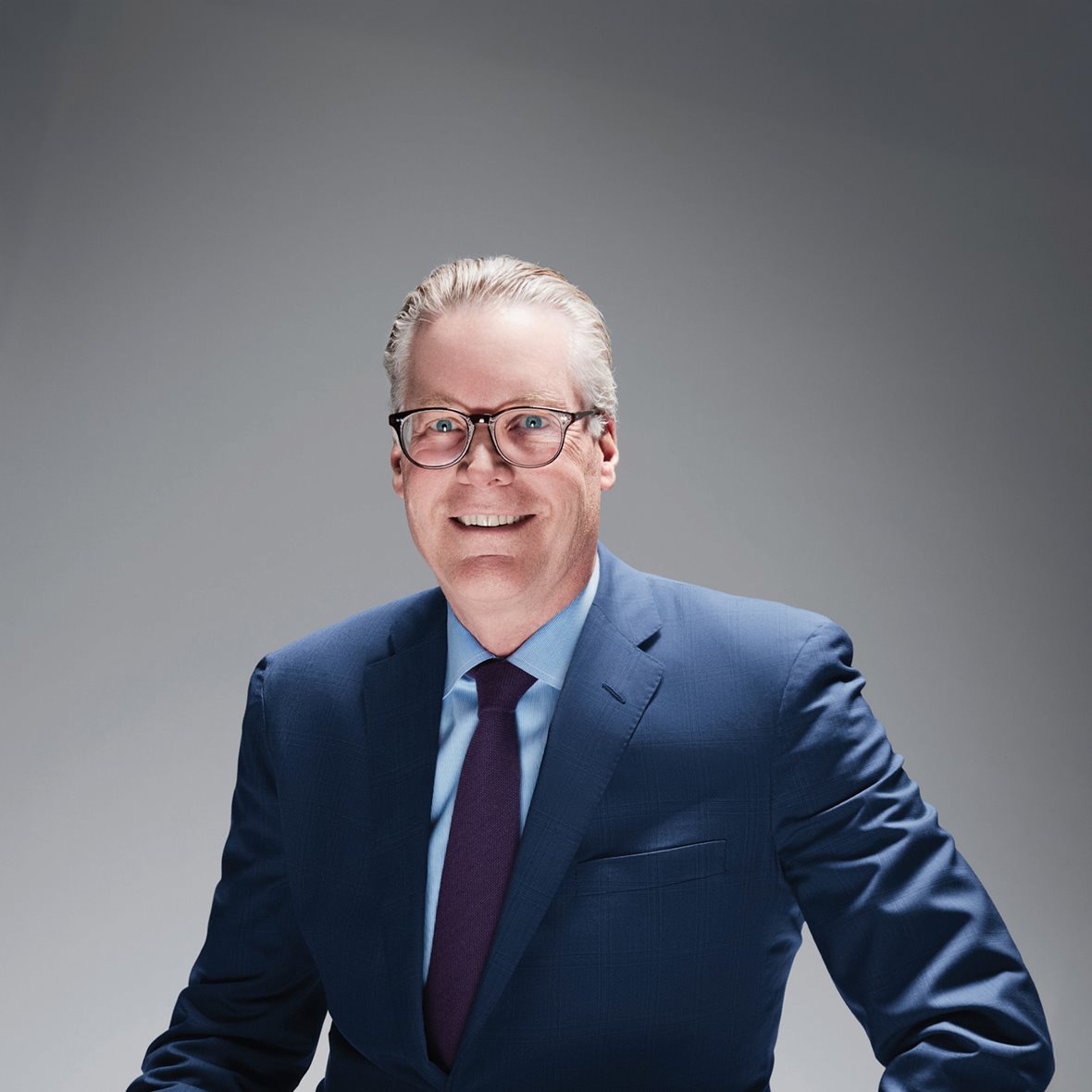 Ed Bastian, sporting a pair of glasses and dressed in a blue suit, light blue shirt, and a purple tie.