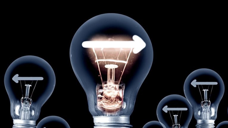 A group of light bulbs set on a dark backdrop. All of the bulbs display a left-facing arrow, except for one bulb that stands out with a right-facing arrow and is illuminated.