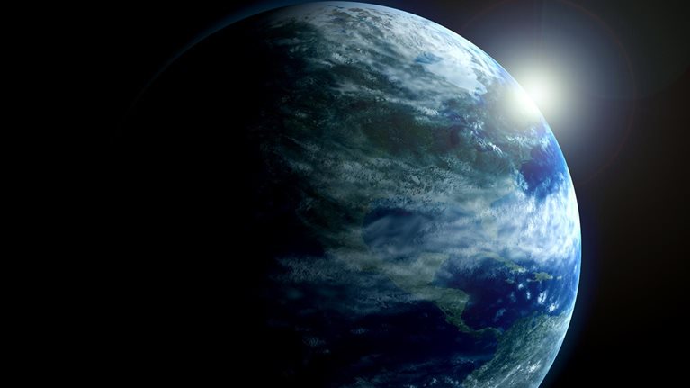 A partially illuminated Earth with the Americas visible as sunlight emerges from behind the planet.