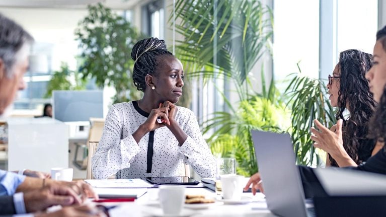 A Black businesswoman sitting at the head of a board room conference table and listening thoughtfully as a colleague shares ideas.