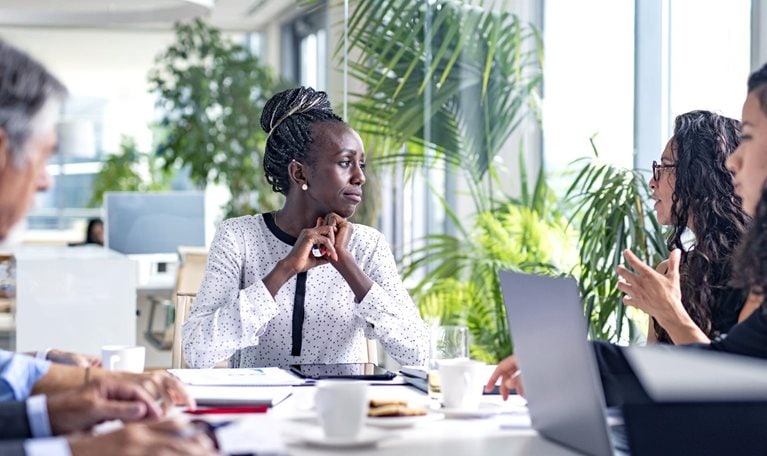 A Black businesswoman sitting at the head of a board room conference table and listening thoughtfully as a colleague shares ideas.