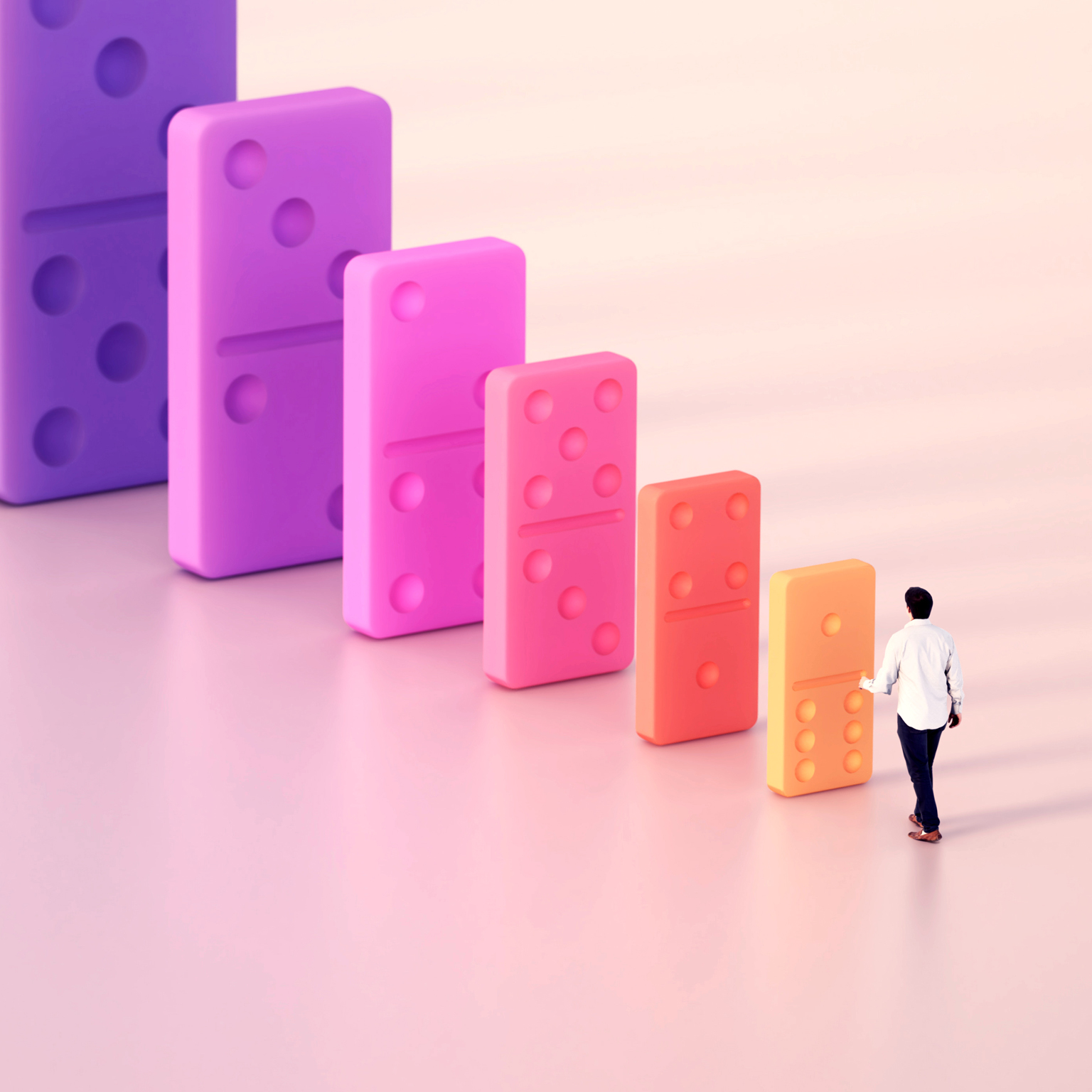 A person approaches a row of increasingly large, colorful dominoes, suggesting a cascading impact.