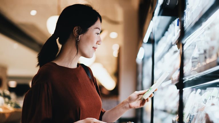 Young Asian woman carrying a shopping basket while grocery shopping in supermarket