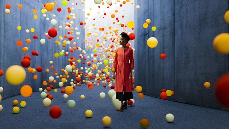 Woman walking in abstract concrete corridor with large amount of exploding spheres.