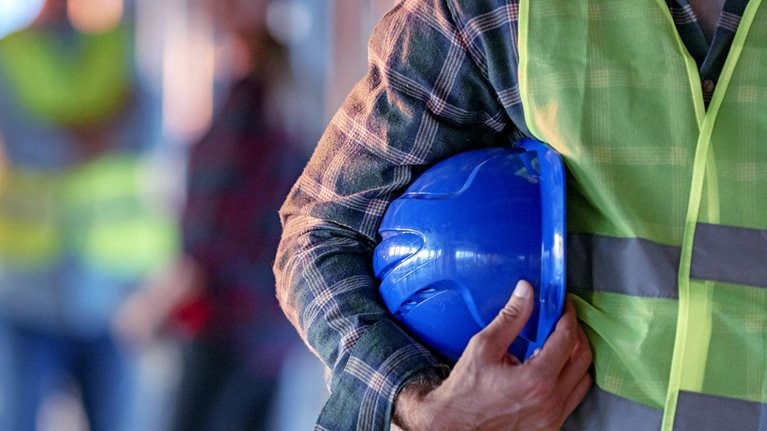 Close-up of worker holding a hardhat with more workers out of focus in the background.