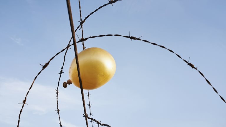 A deflating yellow balloon caught in barbed wire against a gray sky