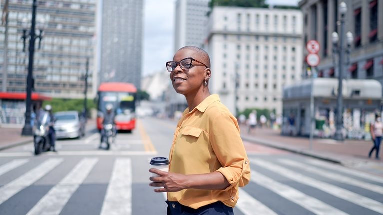 A person crossing the street holding a coffee cup