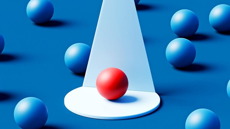 A single red sphere rests on a white circular platform beneath a focused cone of light, standing out vividly among numerous blue spheres scattered across a deep teal background.