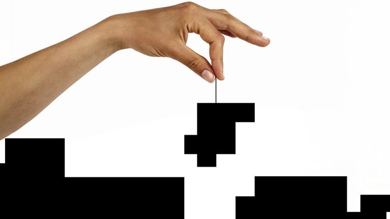 Conceptual image of a hand lowering a puzzle piece into a black and white puzzle.