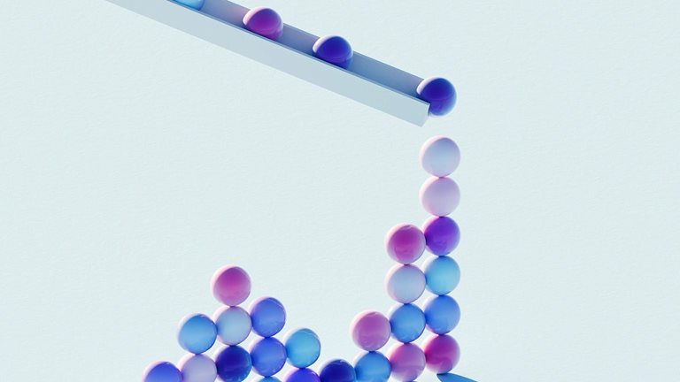 Colorful spheres roll off a slanted track and collect in a rising cluster on a light blue surface.