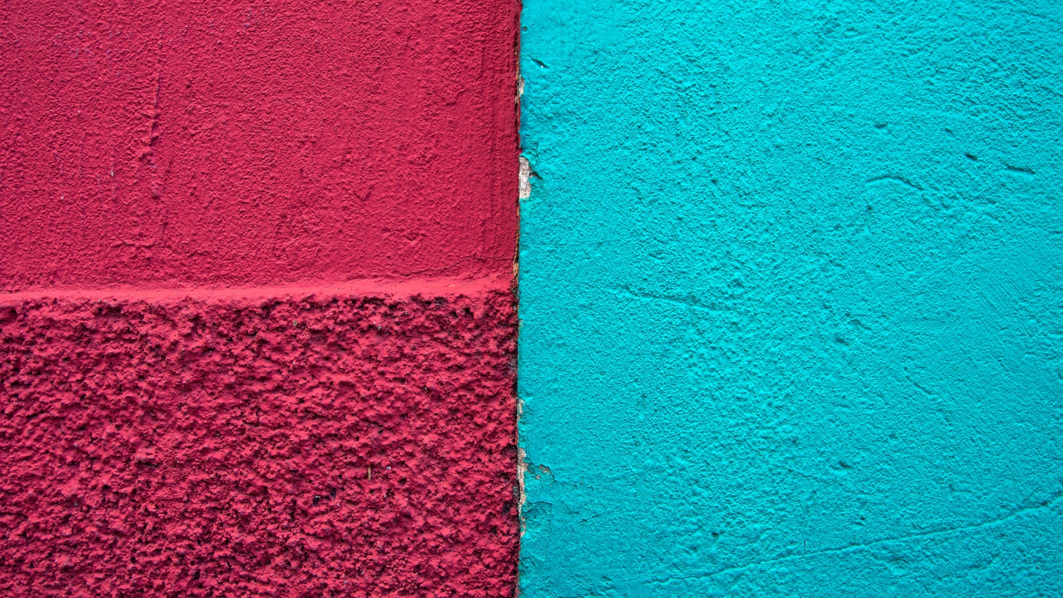 Meeting point of two colonial buildings' stucco exterior walls, one painted deep raspberry red and the other light blue