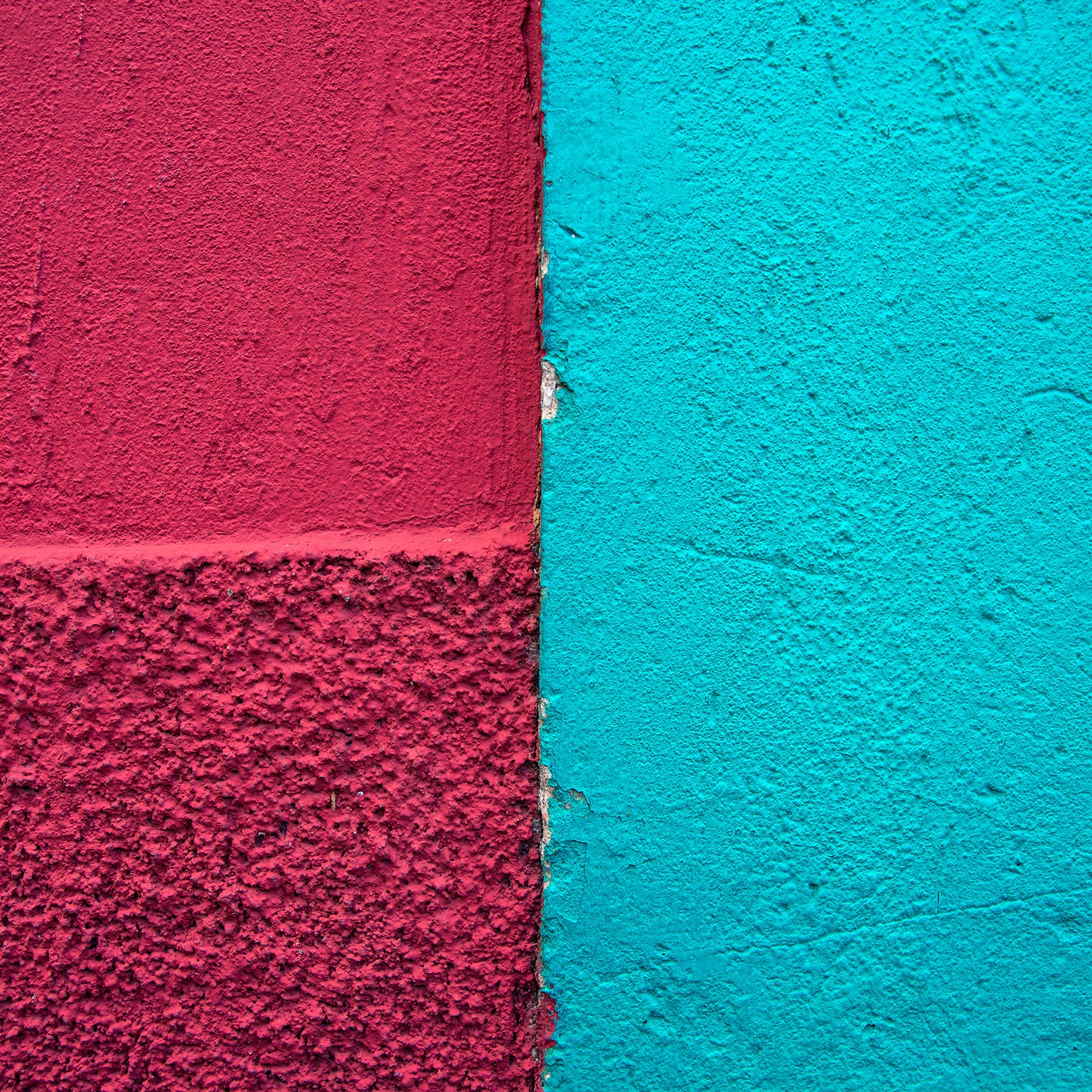 Meeting point of two colonial buildings' stucco exterior walls, one painted deep raspberry red and the other light blue