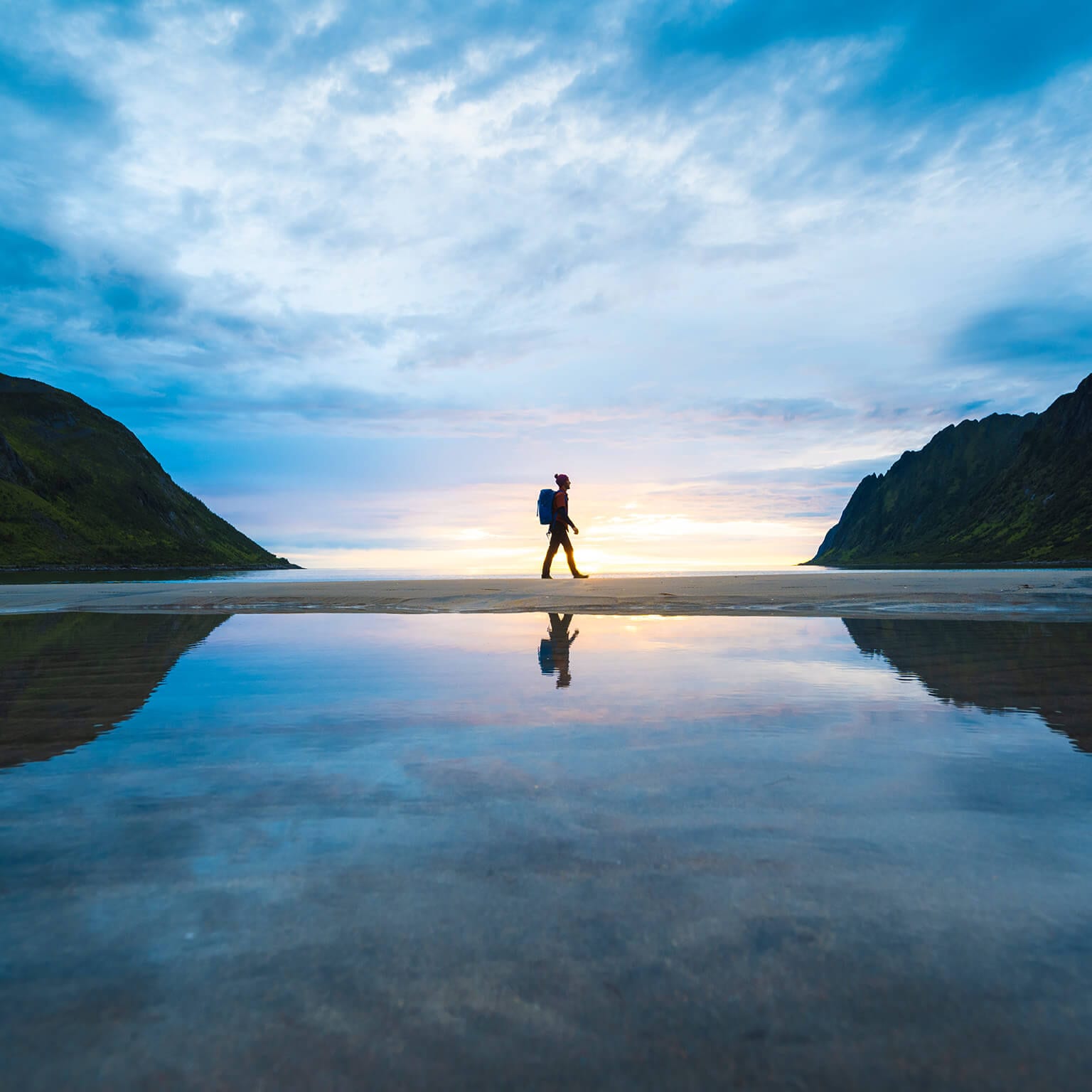 solo backpacker walking along beach, backlit by sunrise