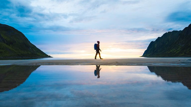 solo backpacker walking along beach, backlit by sunrise