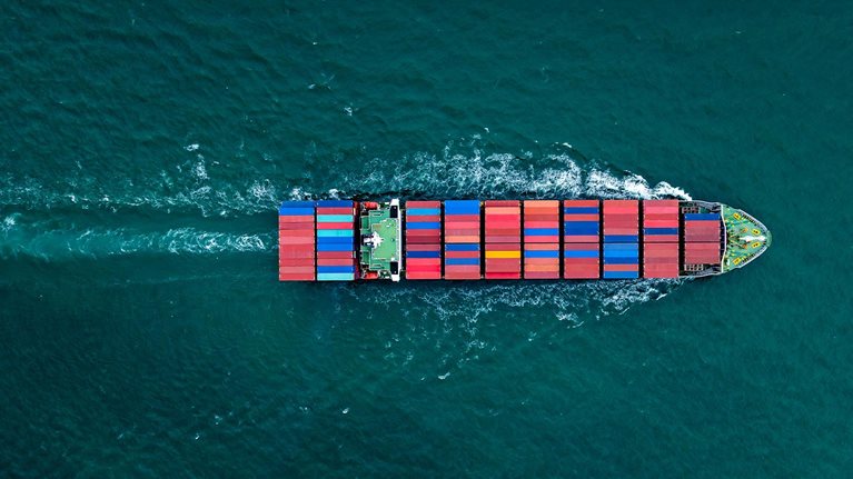 Overhead view of a large container ship sailing with many stacks of colorful containers visible on board