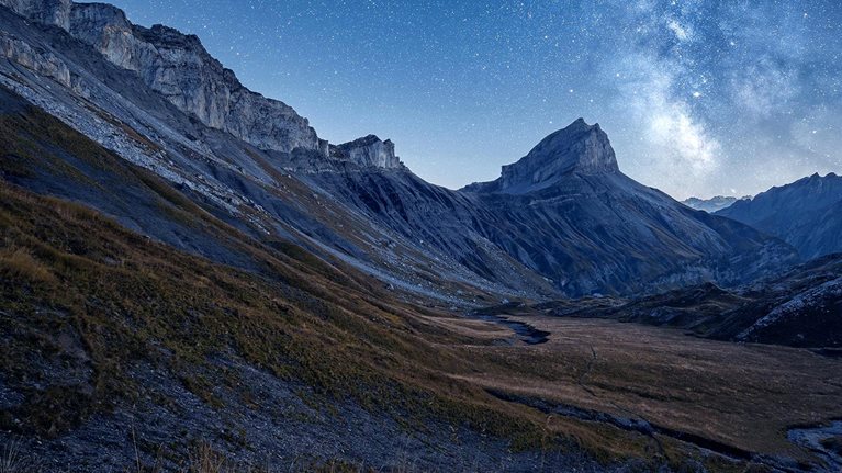 Landscape view of the milky way over dry meadows and a mountain range in the background