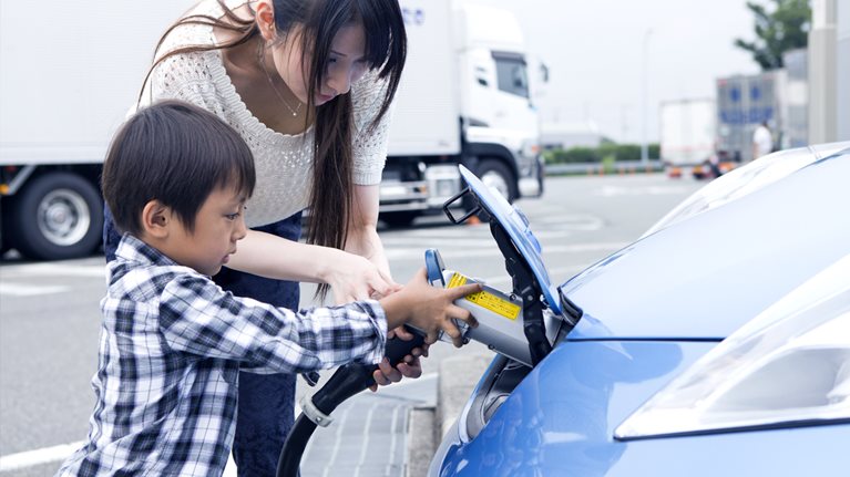 A mother helps her young son as he plugs their electric vehicle into charge