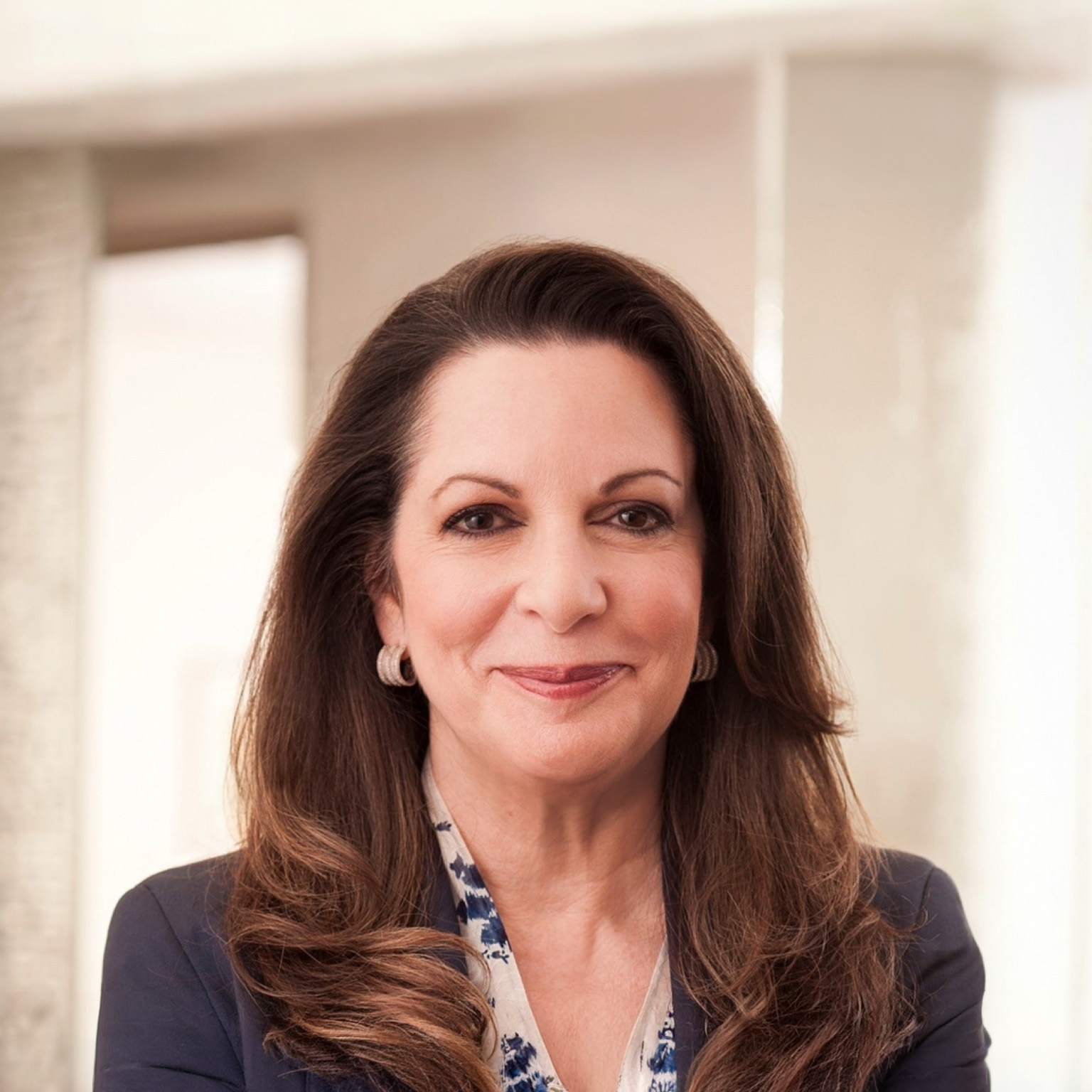 A professional headshot of Julia Stewart. She has long dark brown hair and is wearing a dark blazer over a patterned blouse while smiling gently. 