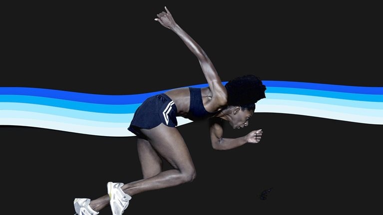 A sprinter launching powerfully from starting blocks against a dark background, her body angled forward in an explosive start. Behind her, a flowing band of layered blue and white stripes creates a sense of motion and energy.