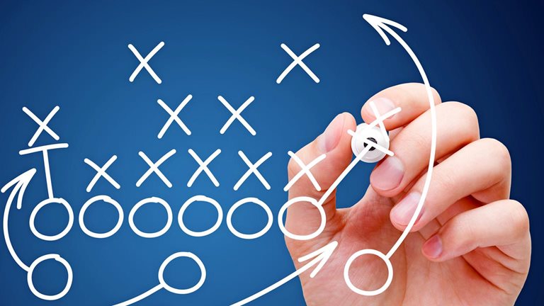 A football play diagram is being sketched by a hand, featuring Xs and Os to represent players and arrows indicating their movements.