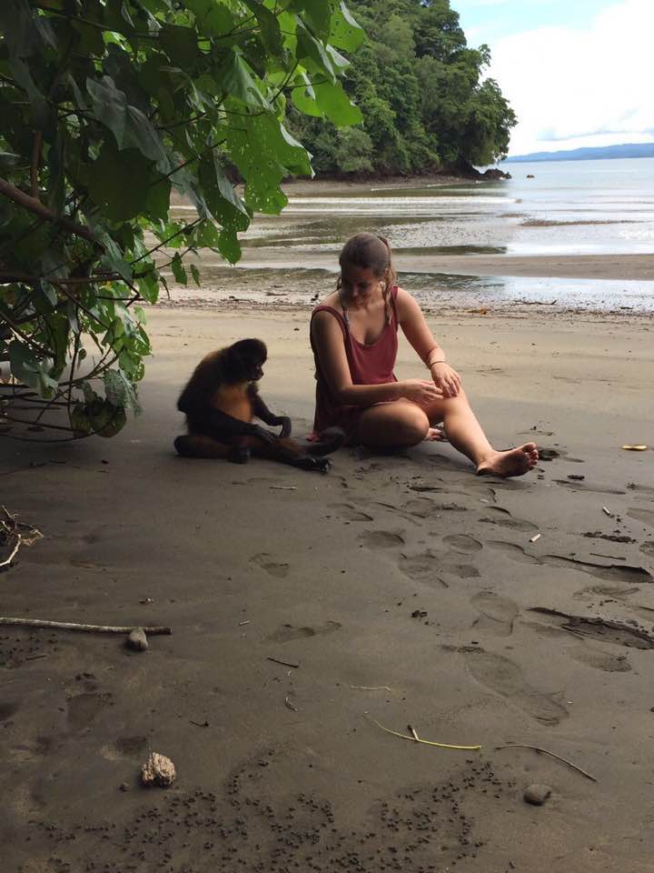 Joana sitting next to a monkey on the beach in Costa Rica