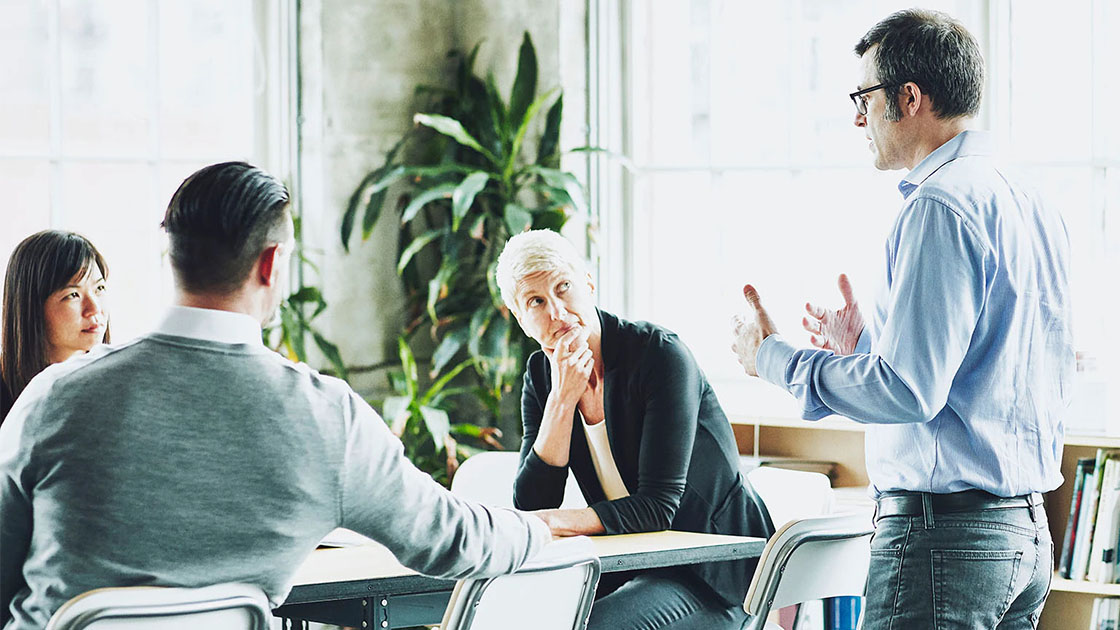 Standing office worker addressing three colleagues