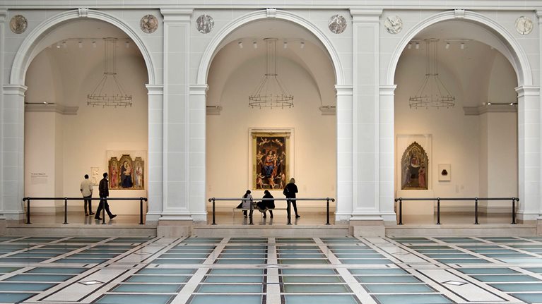 Image of a gallery in a museum, with three arches in the forefront and three exhibits in the background, two of which are flanked by patrons