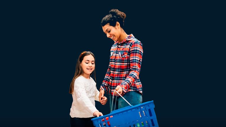 mother holding grocery basket, daughter placing items in - stock photo