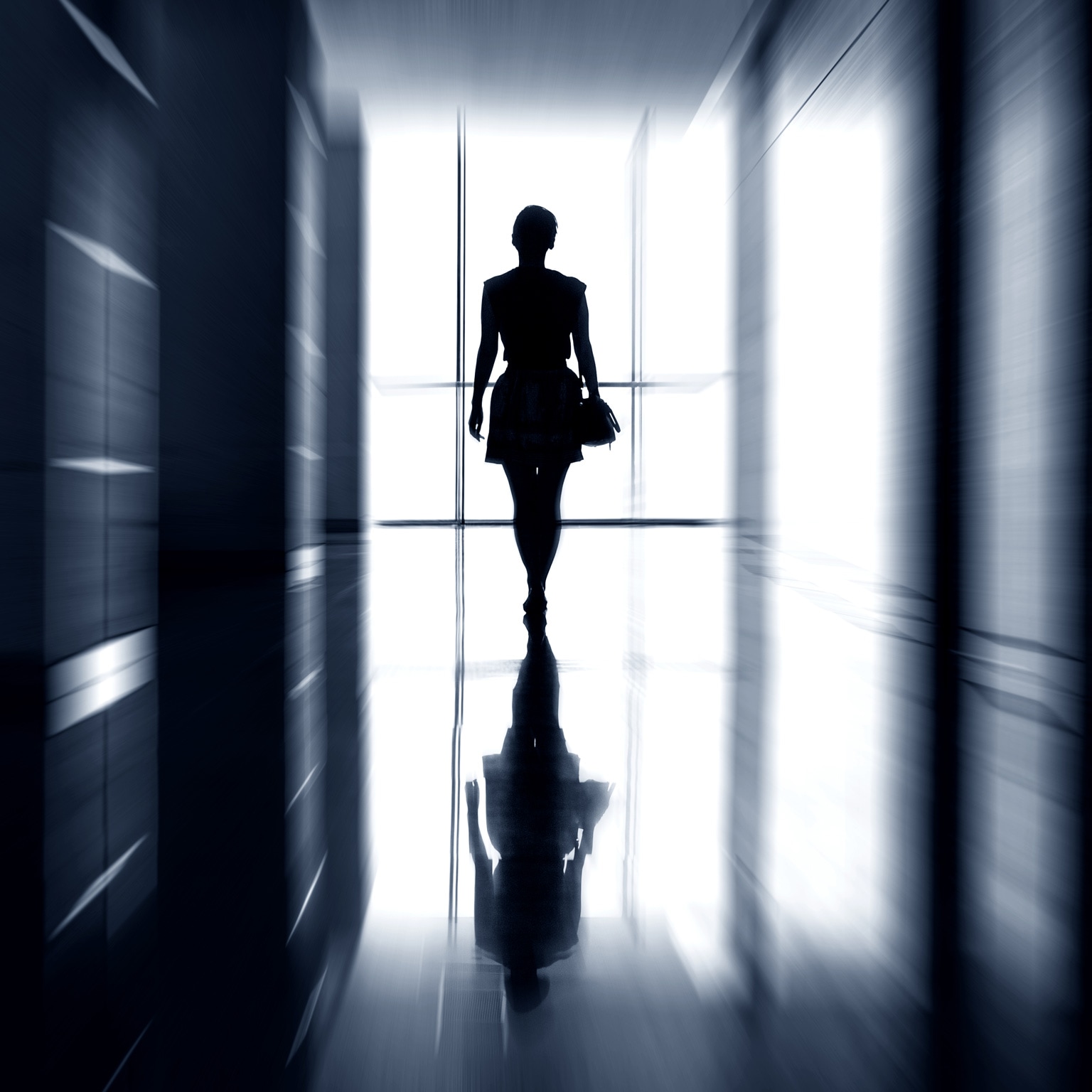 Silhouette of a woman walking away into the light down an office hallway
