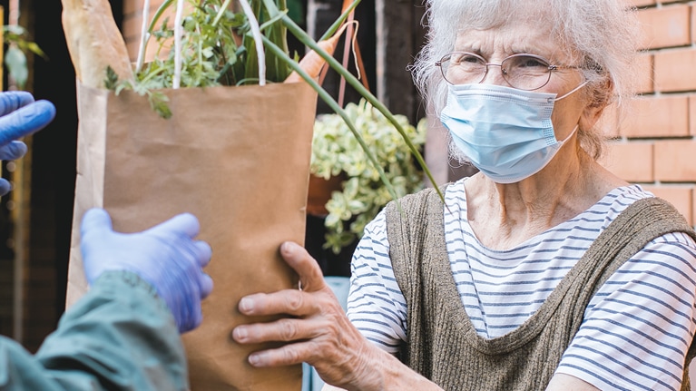 Elderly woman being handed a bag of groceries
