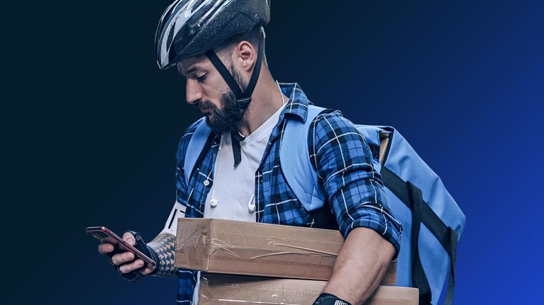 Man in biking helmet holding packages and delivery bag, looking at phone