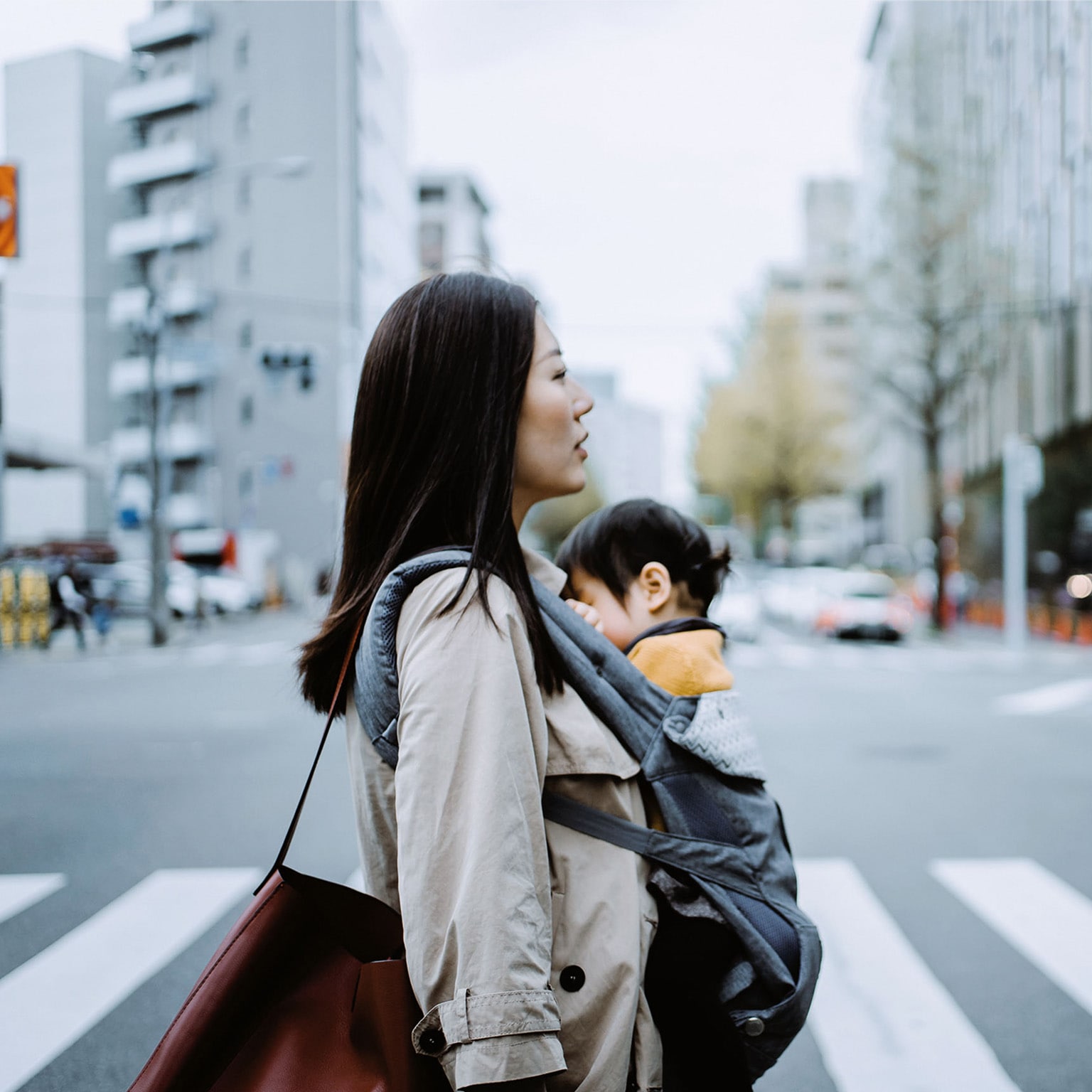 Young Asian working mother crossing street and commuting in busy downtown city with little daughter