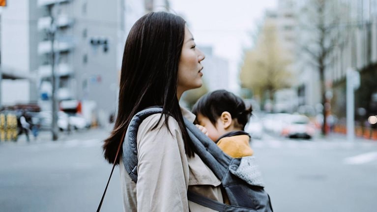 Young Asian working mother crossing street and commuting in busy downtown city with little daughter