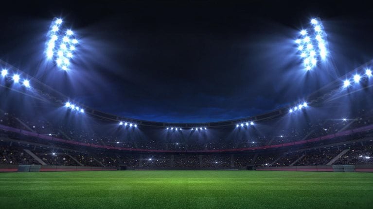 Universal grass stadium illuminated by spotlights and empty green grass playground